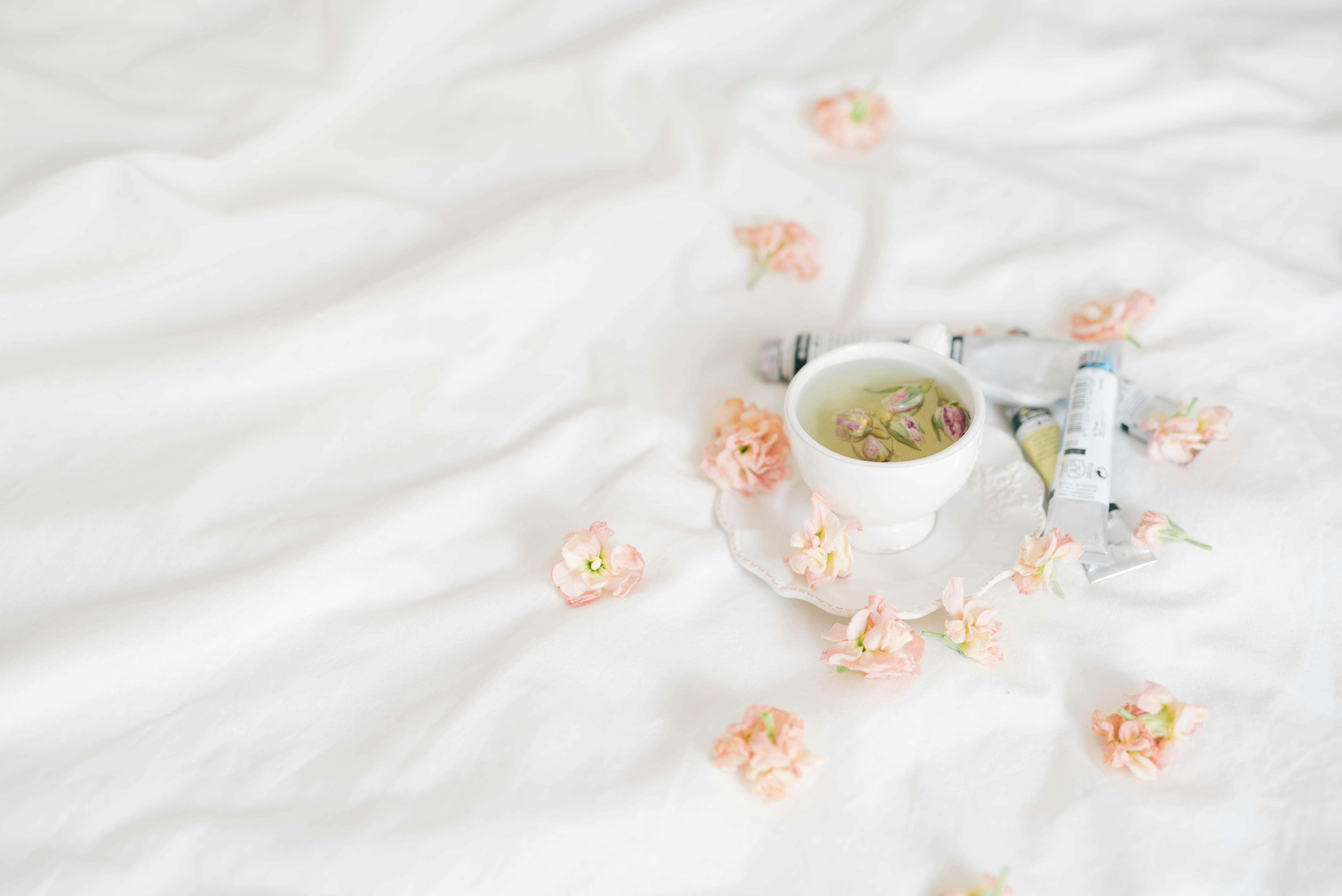 a cup of tea surrounded by petals and tubes of paints on a white surface