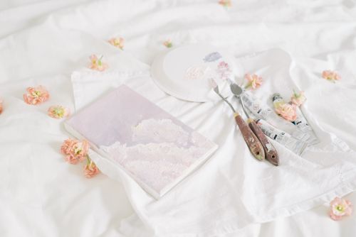 Free Artistic setup with flowers, paint tubes, and palette knives on a white blanket. Stock Photo