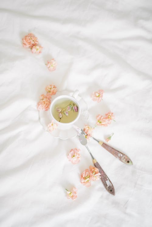 Free Flavored Tea on White Ceramic Cup Surrounded by Petals on White Blanket Stock Photo