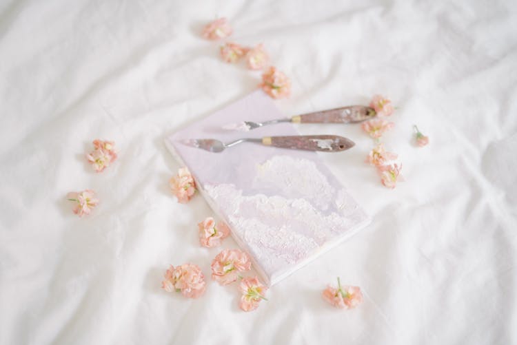 Painting Knives On A Notebook Surrounded By Flower Petals