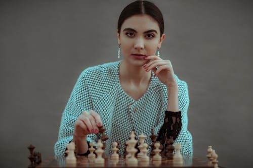 Focused ethnic female player making chess move while playing game at table against gray background