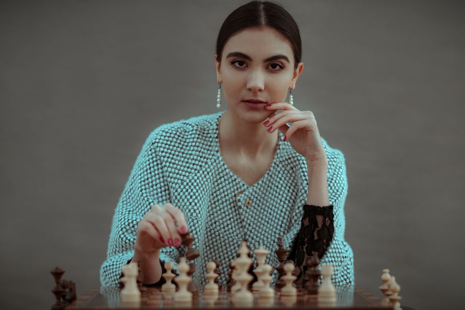 the role of finance in strategic decision-making - Focused ethnic female player making chess move while playing game at table against gray background