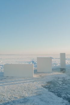 A serene winter landscape featuring minimalist white blocks on a snow-covered ground under a clear blue sky.
