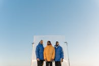 Men Wearing Puffer Jackets Standing Under the Clear Blue Sky