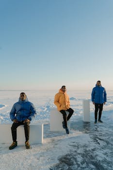 Three men in colorful puffer jackets pose on a snowy landscape under a clear blue sky.