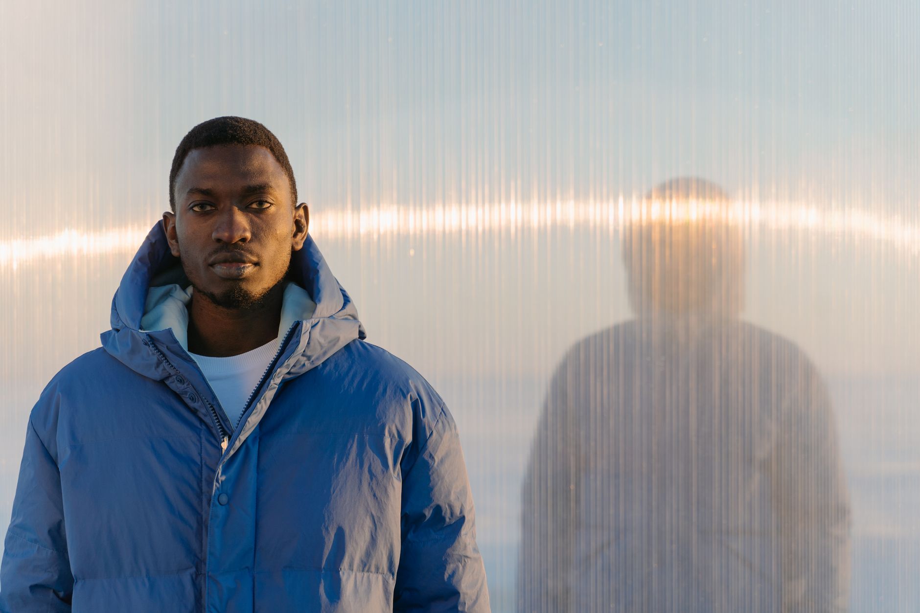 Chic portrait of a man in a blue puffer jacket against frosted glass with warm light.