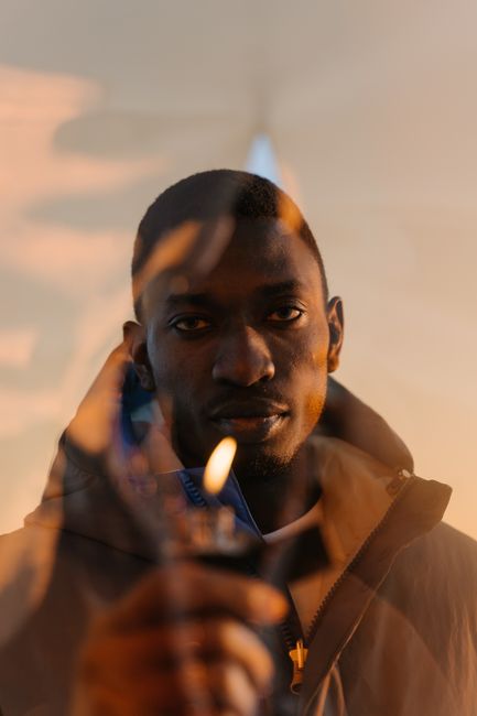 A man stands holding a lighter against a plastic curtain with a serious expression.