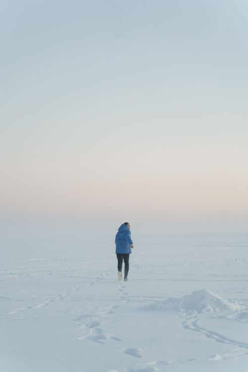 Free Adult in blue jacket running on a vast snow-covered field under a clear winter sky. Stock Photo
