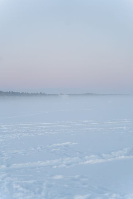 A tranquil snow-covered field with fog under a pastel sky at dawn.