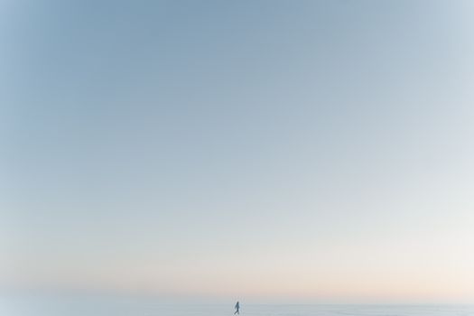 A lone person walks across a wide, snowy expanse under a clear winter sky.