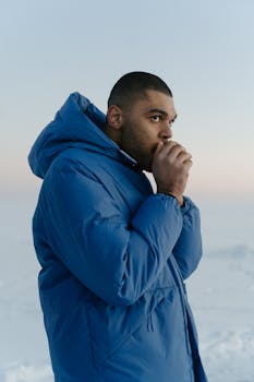 Profile of a man in blue puffer jacket against a snowy backdrop, exhaling warmth.