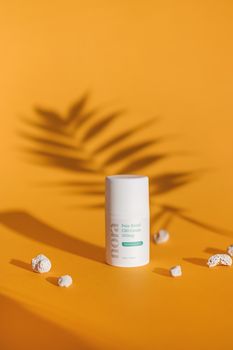 CBD cream in a white container on a yellow backdrop with shadow effects.