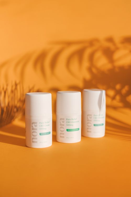 Free Three CBD cream containers on an orange backdrop with shadows, promoting a natural and calming product aesthetic. Stock Photo