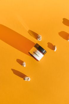 Amber jar of beauty product with shadow and stones on a bright orange background.