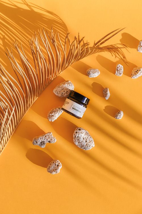 Free A minimalist arrangement featuring a product jar with dried palm leaf and stones on a vibrant orange background. Stock Photo