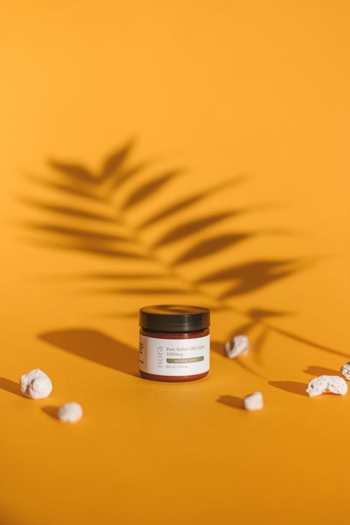 Free Cosmetic jar on an orange surface with leaf shadow, showcasing vibrant product photography. Stock Photo