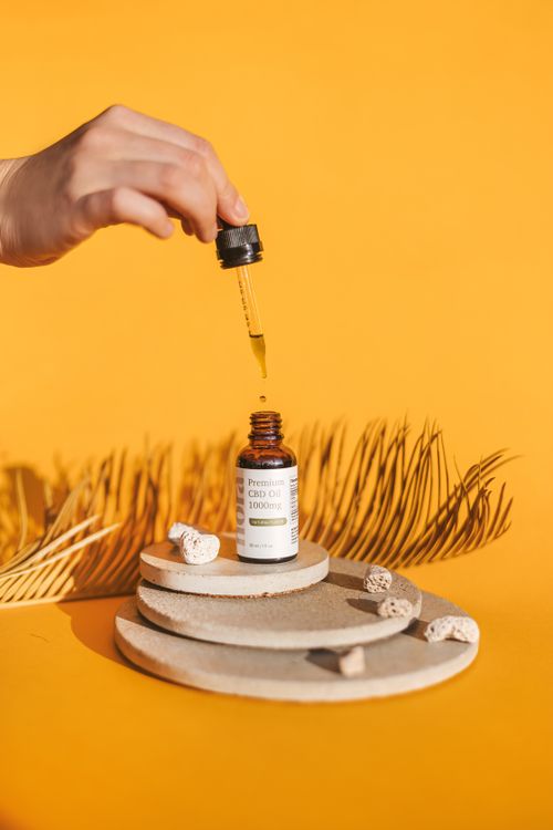 Free Close-up of hand using dropper to dispense CBD oil into bottle on bright yellow background. Stock Photo