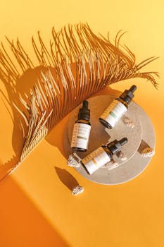 Aesthetic display of skincare serum bottles with palm leaf shadow on vibrant yellow backdrop.