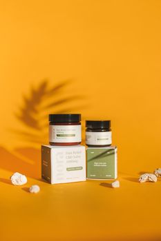 Product photography of CBD salve jars and boxes on an orange background with shadow effects.
