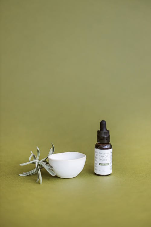 CBD Oil Bottle and Small Bowl on Green Background