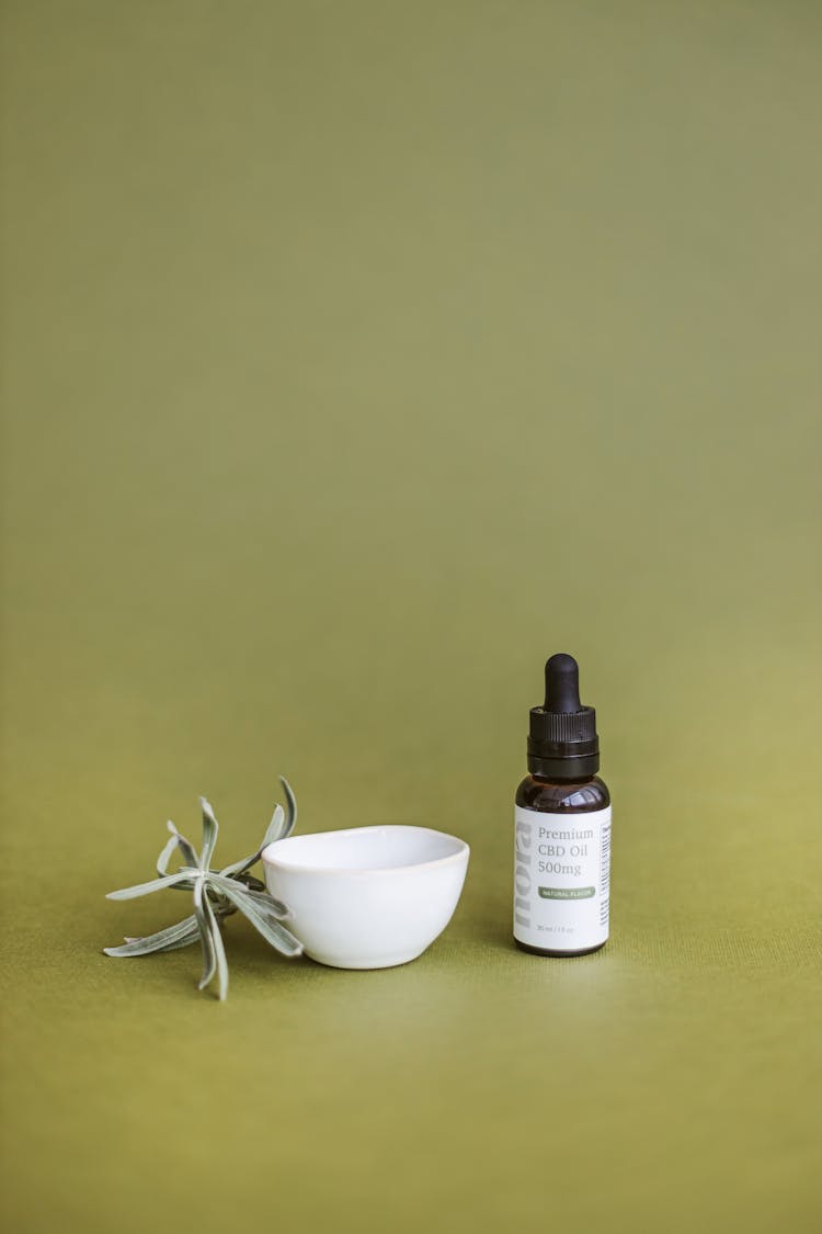 CBD Oil Bottle And Small Bowl On Green Background