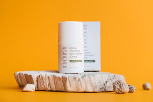 Close-up of a CBD eczema treatment ointment on a rustic platform against a yellow backdrop.