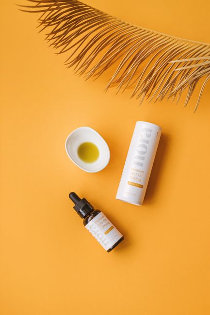 A CBD oil bottle and packaging set against a yellow background with palm leaf accent.