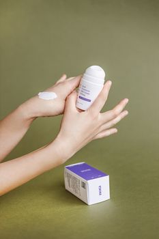 A close-up shot of hands applying moisturizing cream from a bottle against a green background.