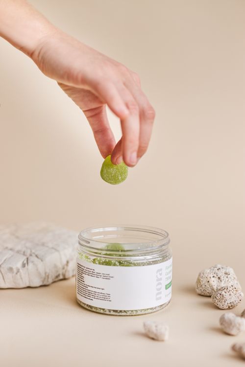 Free A hand holding a green gummy above an open jar on a minimalist background. Stock Photo