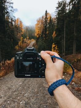 A DSLR camera held by a traveler capturing a scenic autumn forest path in Karelia, Russia.