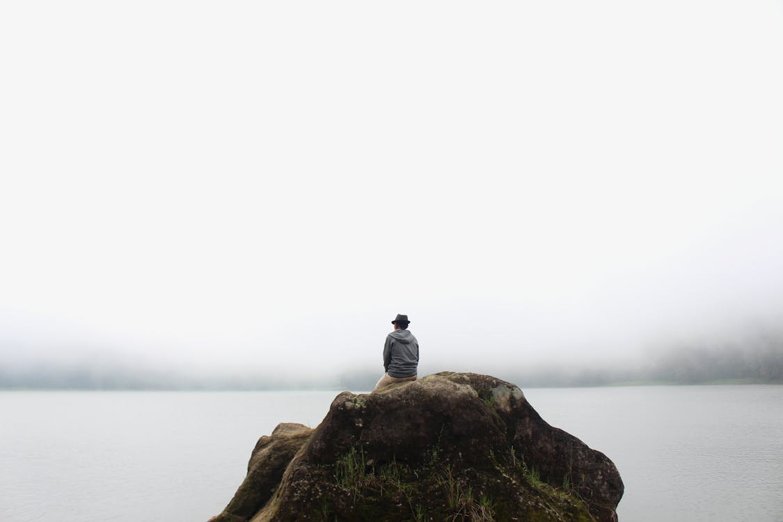 Person Sitting on Rock Near Body of Water