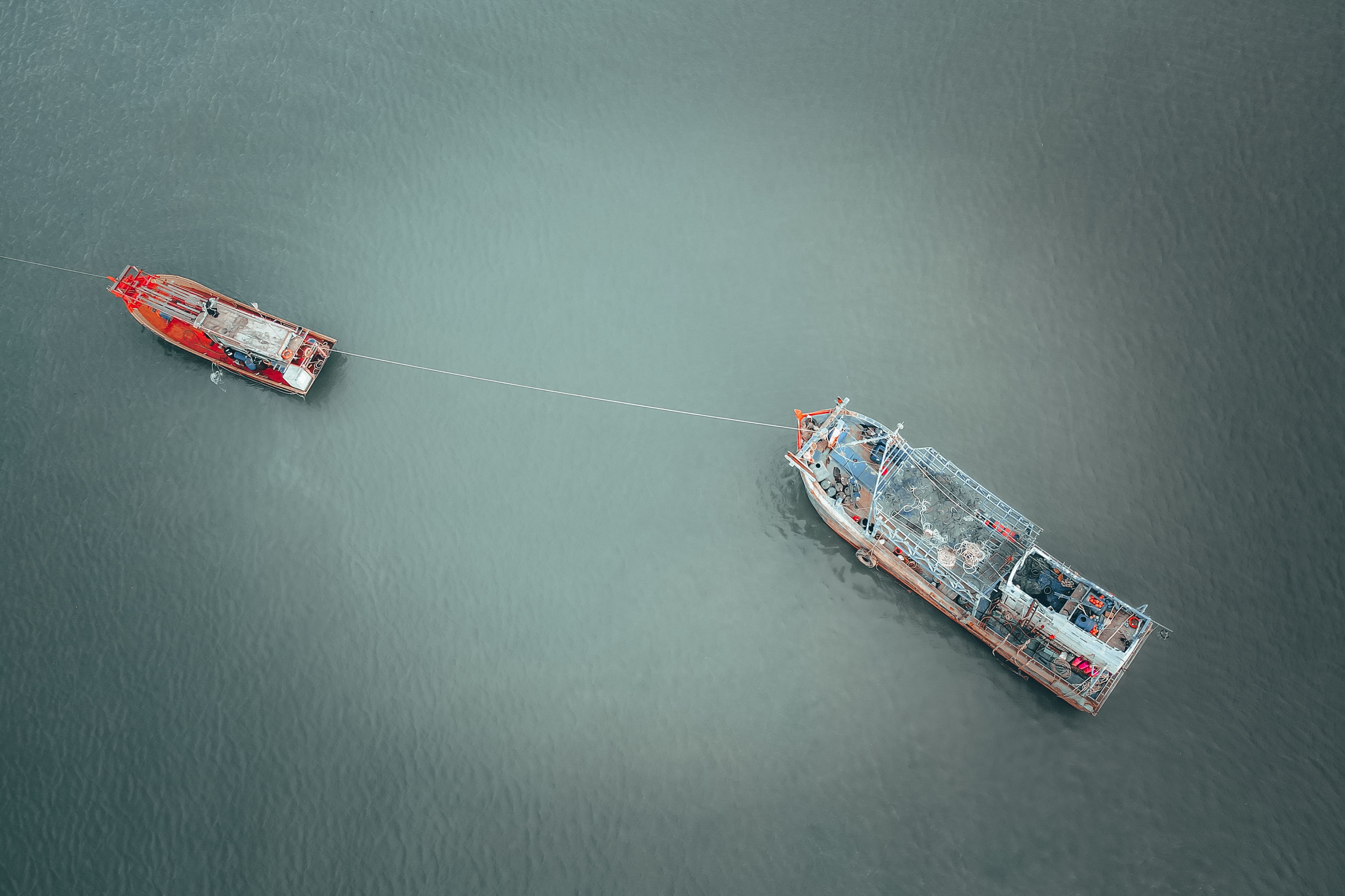 Drone view of barge with cargo and fishing tackle on rope with boat on river
