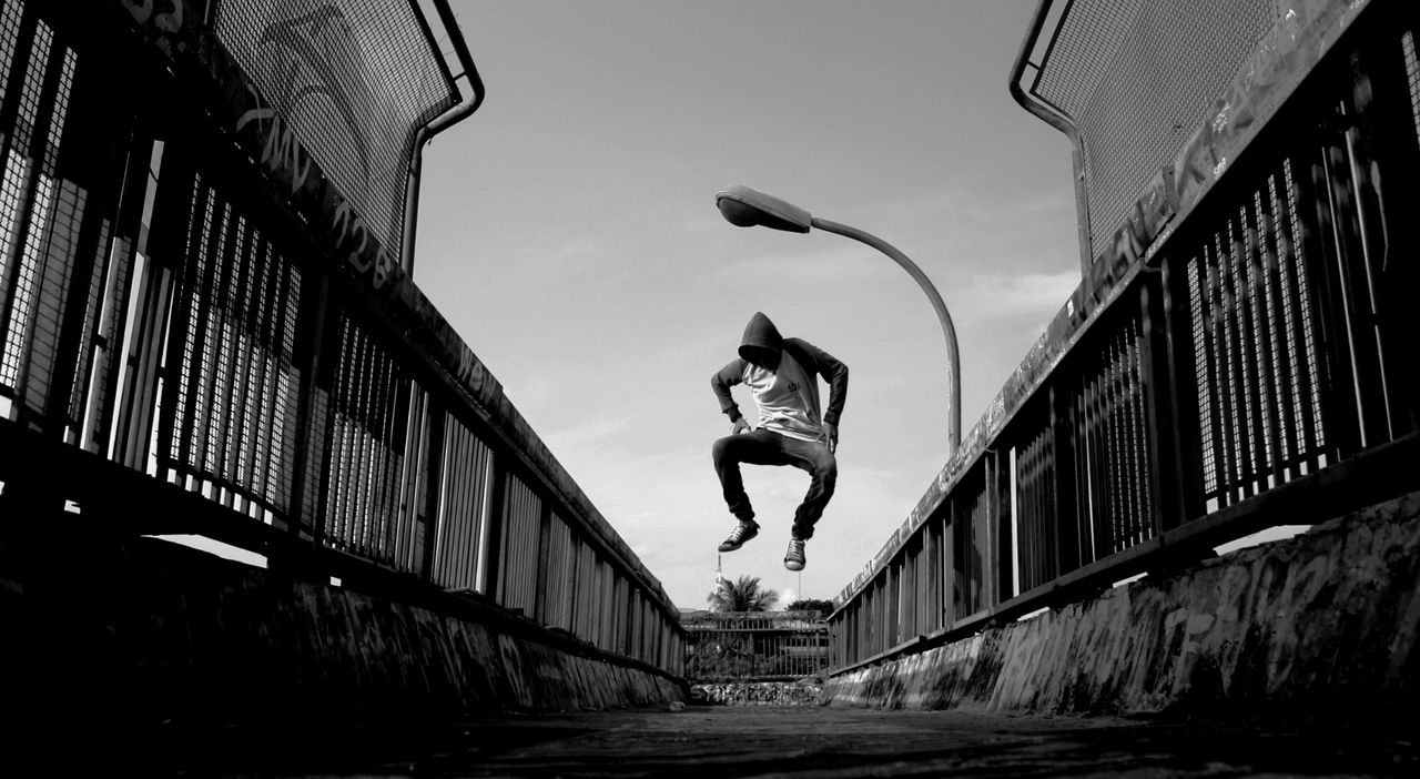 a man in a hoodie jumps lively on an urban bridge in black and white
