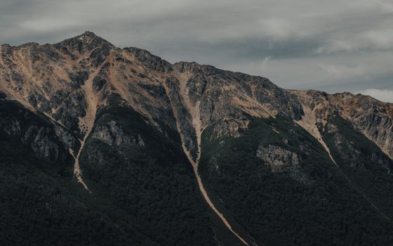 Explore the rugged peaks of a dramatic mountain range beneath a moody cloudy sky.