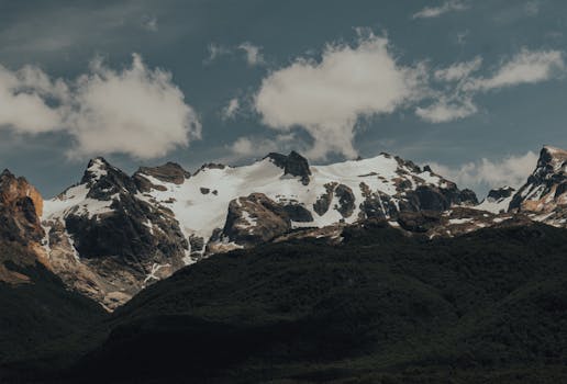 Scenic view of snow-capped rocky mountains with clouds and greenery below.