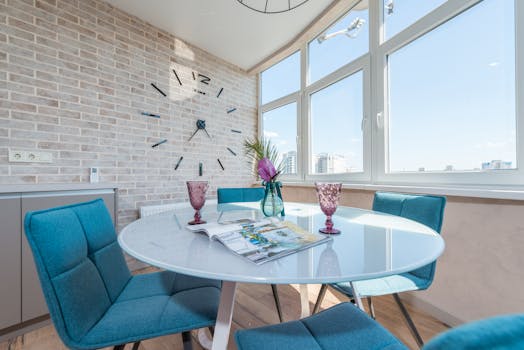 Bright dining area with blue chairs, a round table, and a large wall clock.