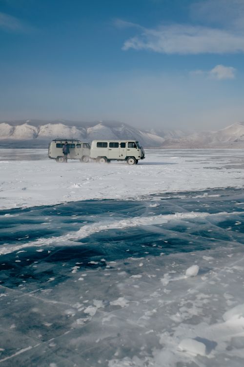 Free A vintage van navigates the icy surface of Lake Baikal under a clear blue sky in a winter landscape. Stock Photo