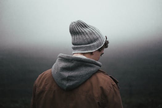 Back view of a young man wearing a beanie and hoodie in a foggy setting, reflecting solitude.