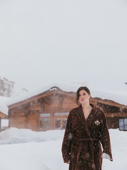 Woman wearing a coat standing outside a snowy chalet in winter, exuding calmness and self-care.