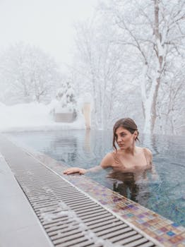 A woman enjoying a warm swim in an outdoor heated pool surrounded by snow-covered trees.