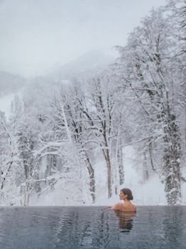 A woman enjoys a warm swim in an infinity pool surrounded by a snowy landscape.
