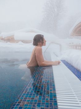 Woman enjoying a snowy day in an outdoor heated pool, embracing winter tranquility.