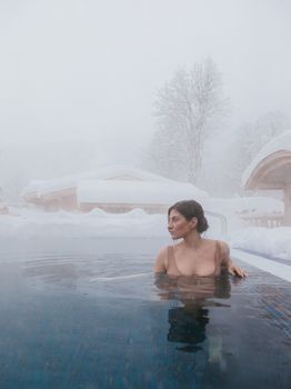 A woman enjoys a warm hot tub surrounded by snow and fog, creating a serene winter scene.
