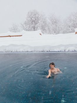 A woman swims in an outdoor pool surrounded by snow-covered ground and trees.