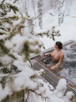 A woman enjoying a warm soak in an outdoor pool surrounded by snow-laden trees.