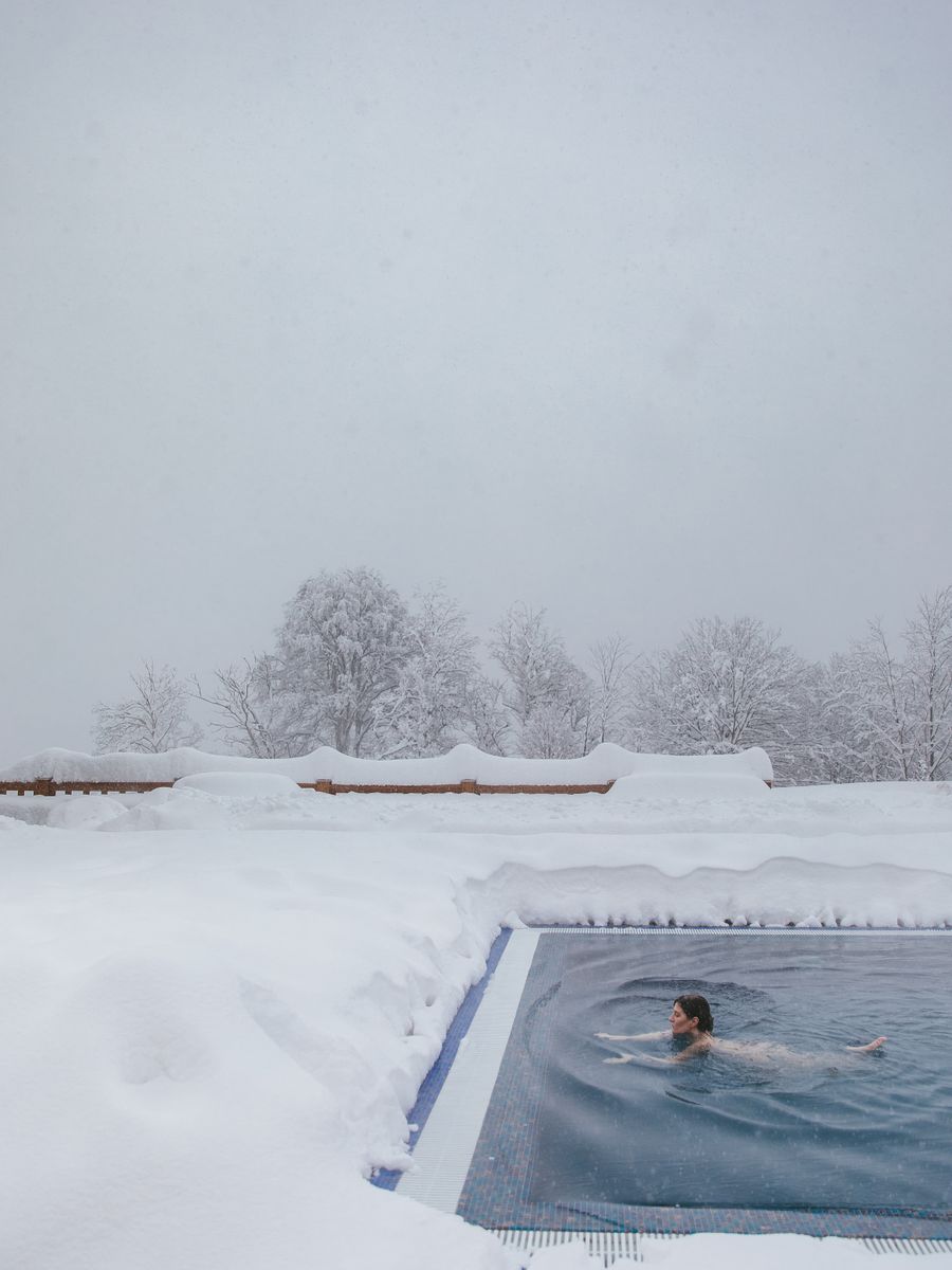 Person swimming in an outdoor pool surrounded by snow for cold exposure therapy