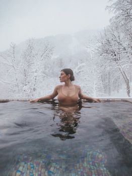 A woman enjoys a relaxing dip in an outdoor pool surrounded by snowy winter scenery.