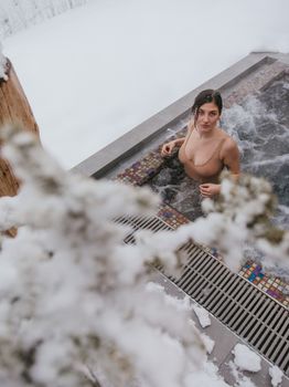 Relaxed woman in an outdoor jacuzzi surrounded by snow in winter.