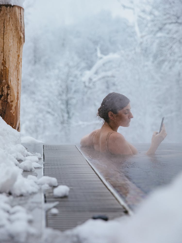 A Woman Soaking On A Jacuzzi While Using Her Cellphone During Winter