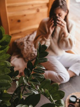 Woman enjoying a warm tea moment indoors surrounded by green foliage.